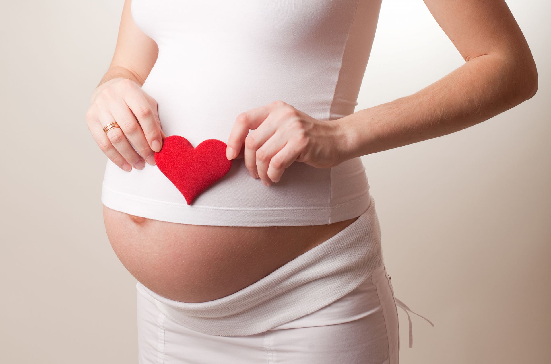 nainen pitelee sydänkoristetta raskausvatsan päällä