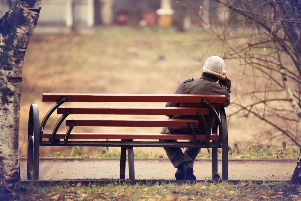 Yksinäinen mies istuu puistonpenkillä