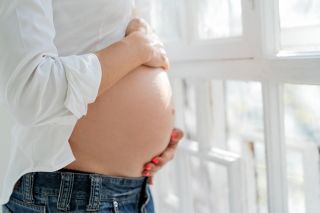 raskaana oleva pitelee vatsaansa ikkunan ääressä