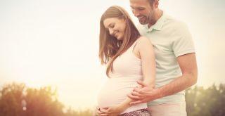 Mies ja raskaana oleva nainen hymyilevät ulkona