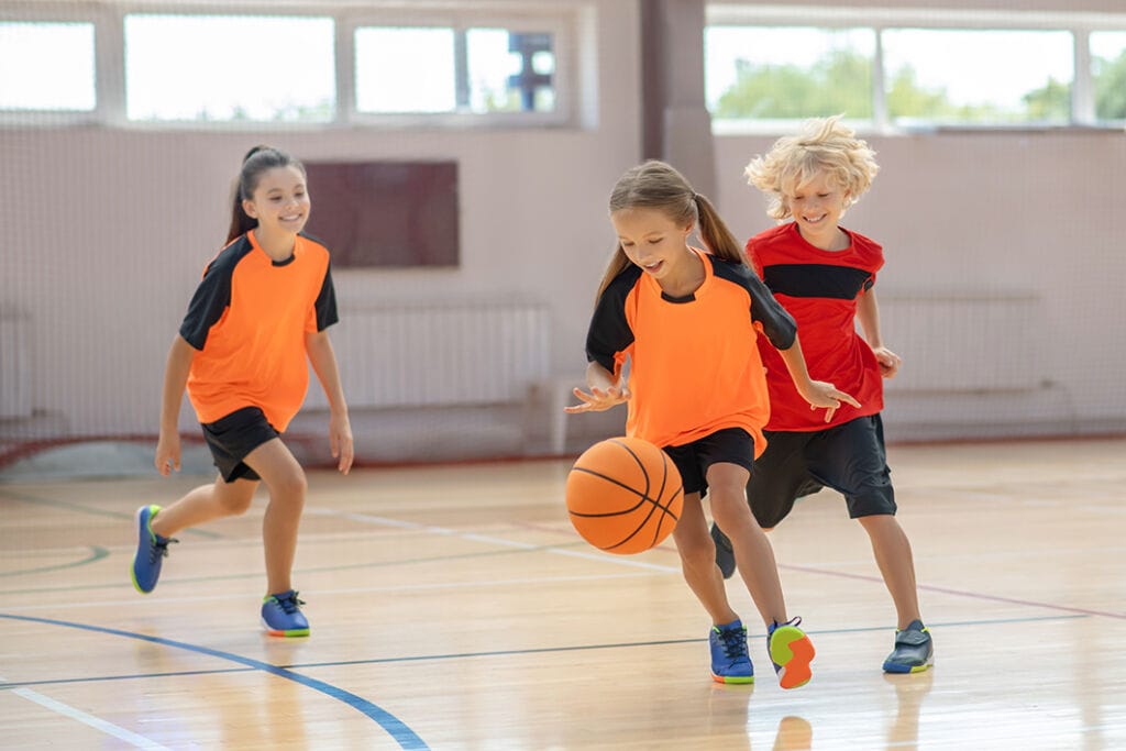 Lapset pelaamassa koripalloa liikuntasalissa