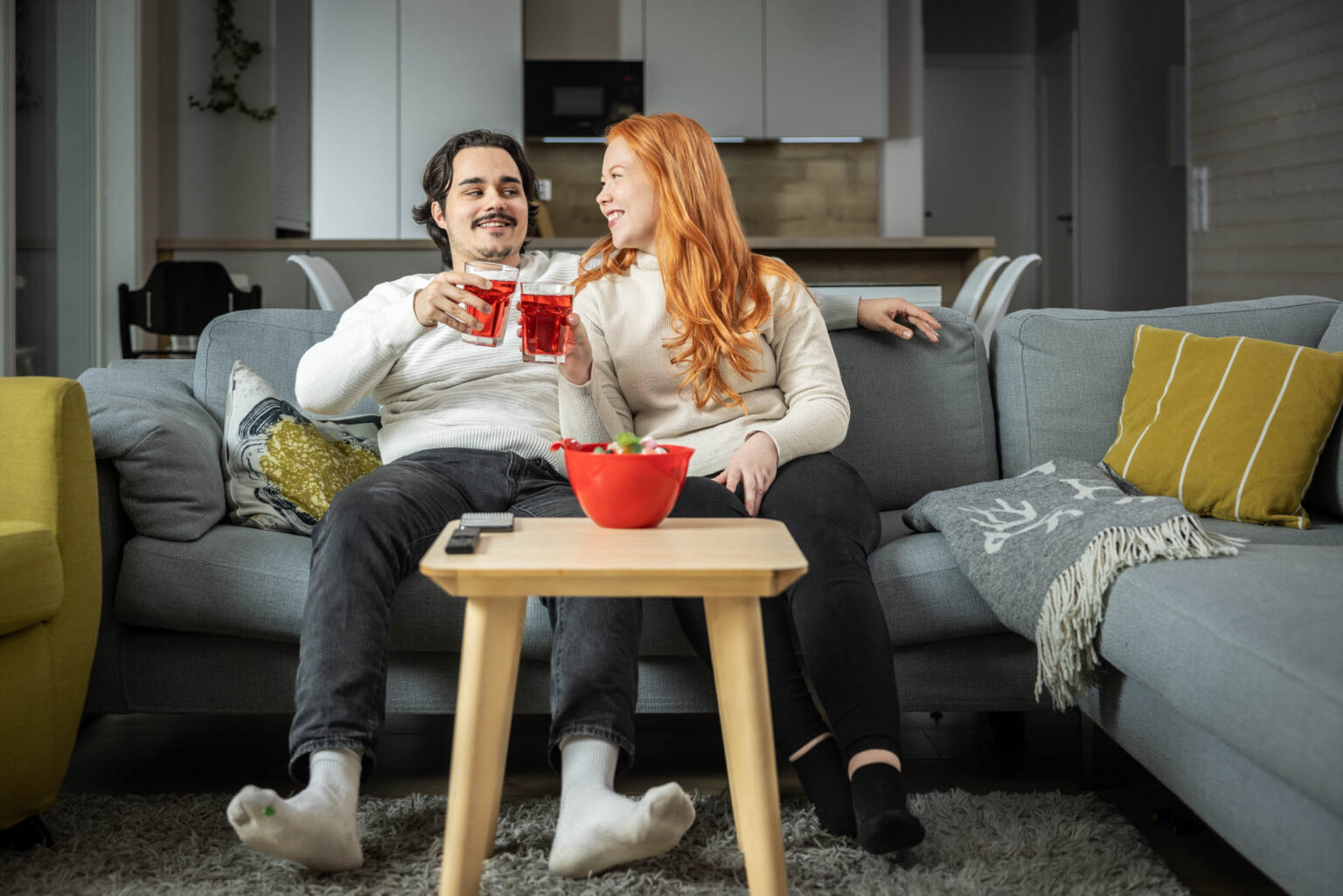 mies ja nainen istuvat sohvalla ja skoolaavat mehulaseilla