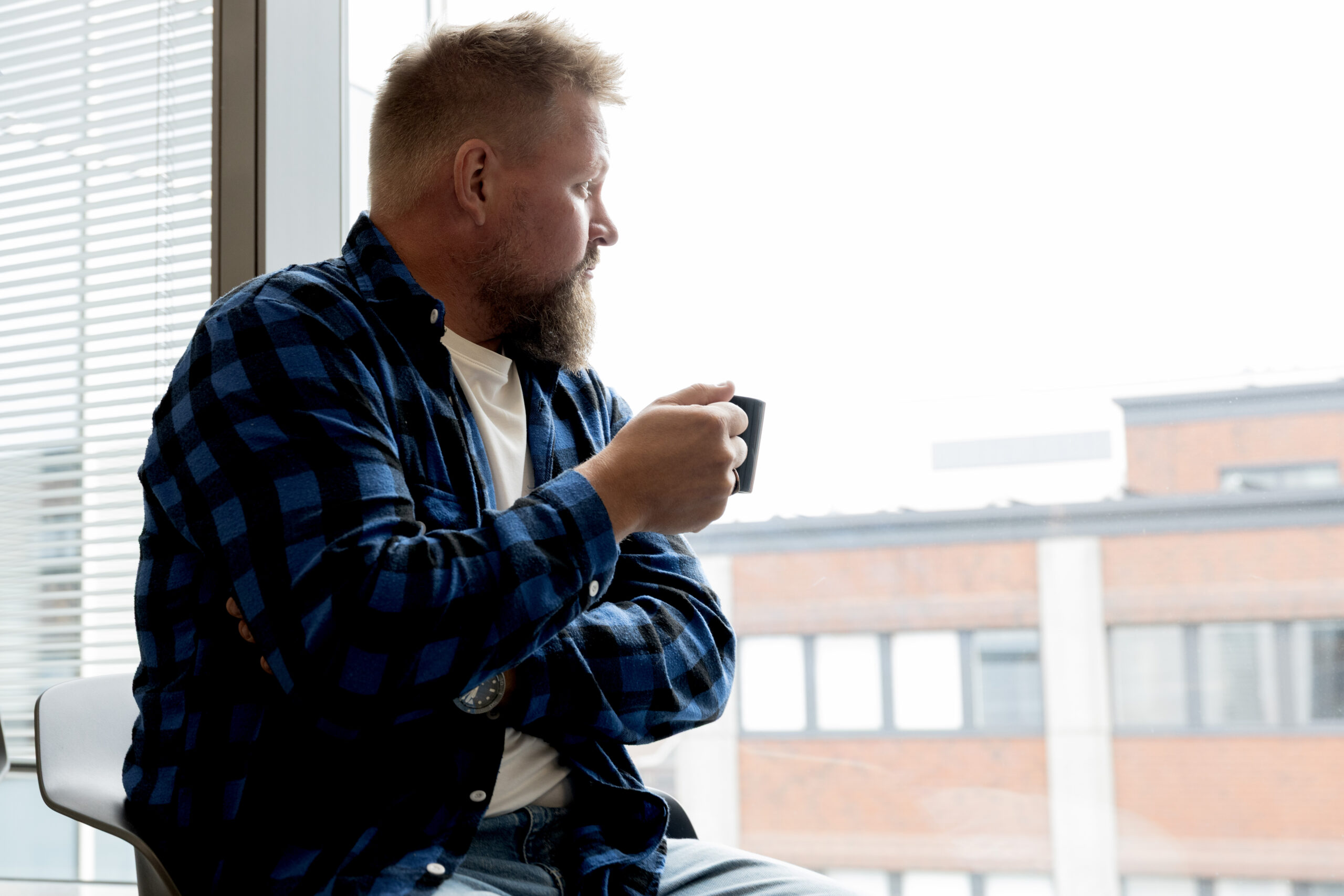 Mies katselee ikkunasta kahvikuppi kädessä